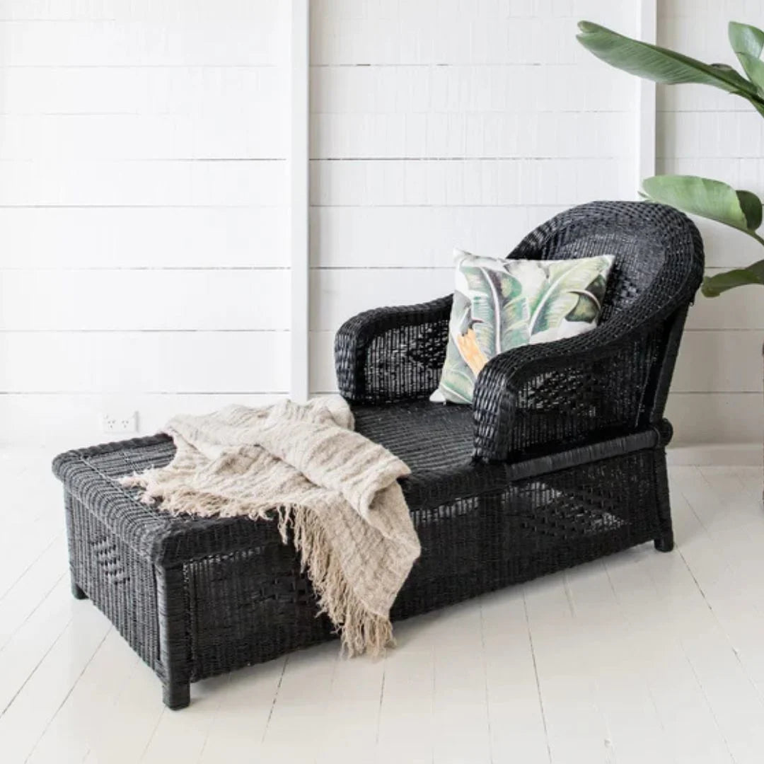 Black wicker chair with a blanket and pillow on a white floor and wall background