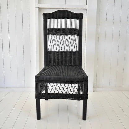Black wicker chair next to a potted plant on a white wooden floor.