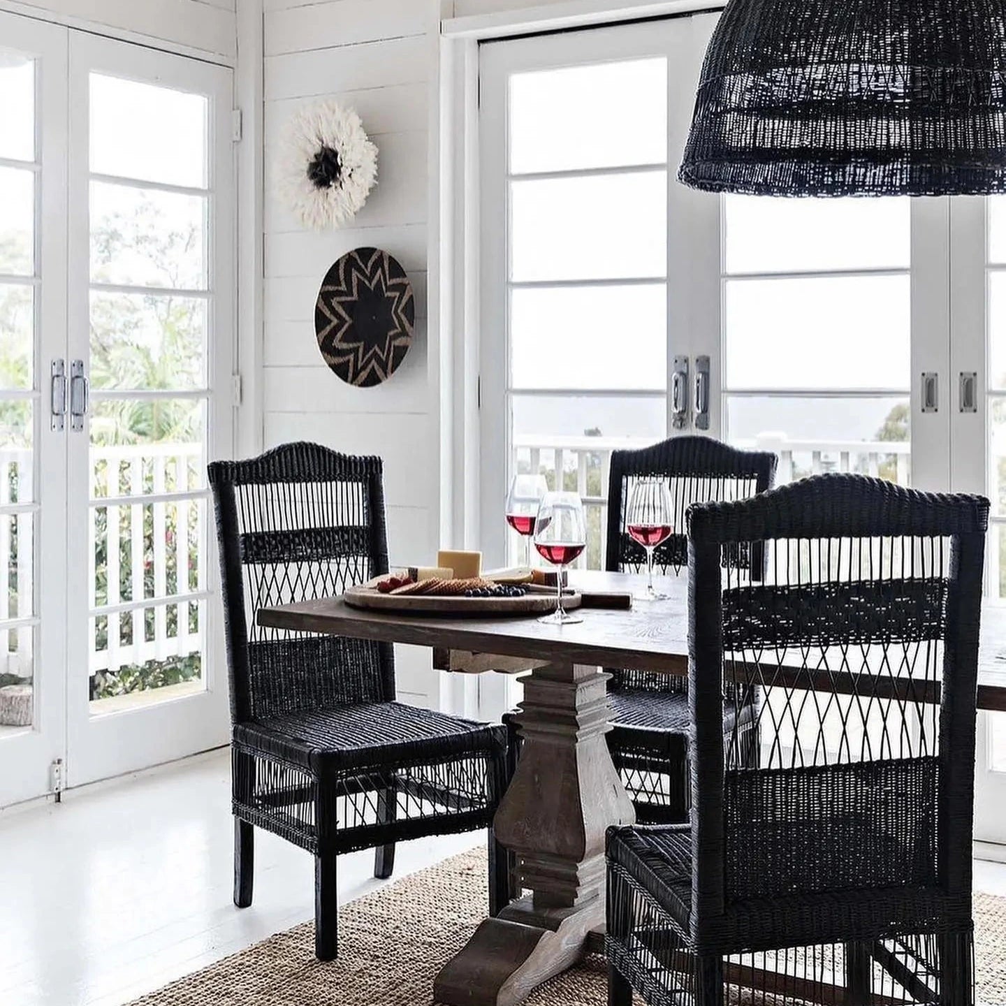Dining area with black wicker chairs and a round table near large windows.