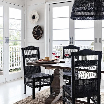Dining area with black wicker chairs and a round table near large windows.