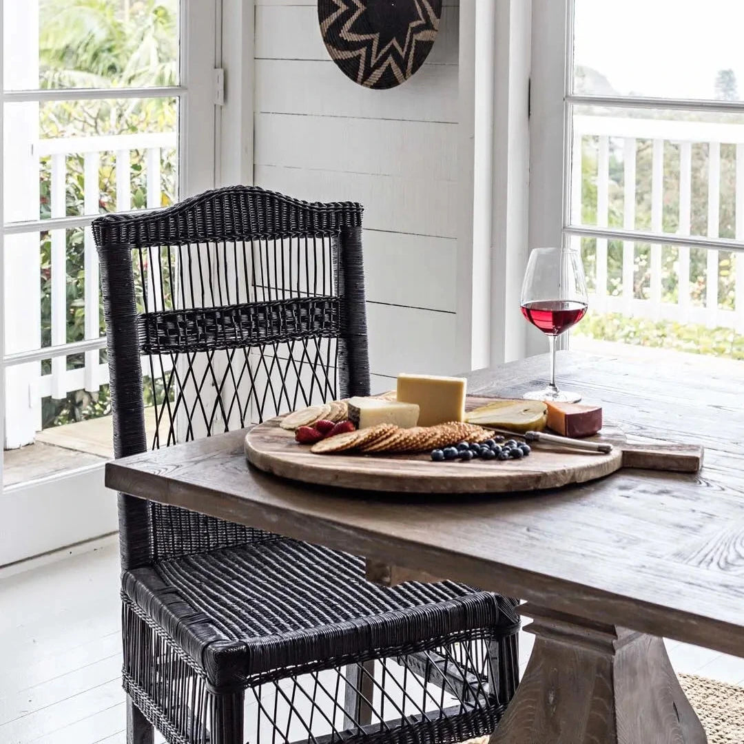Dining area with a wooden table, black wicker chair, and a glass of red wine.