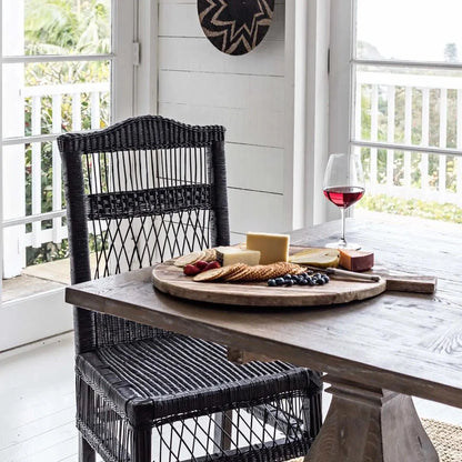 Dining area with a wooden table, black wicker chair, and a glass of red wine.