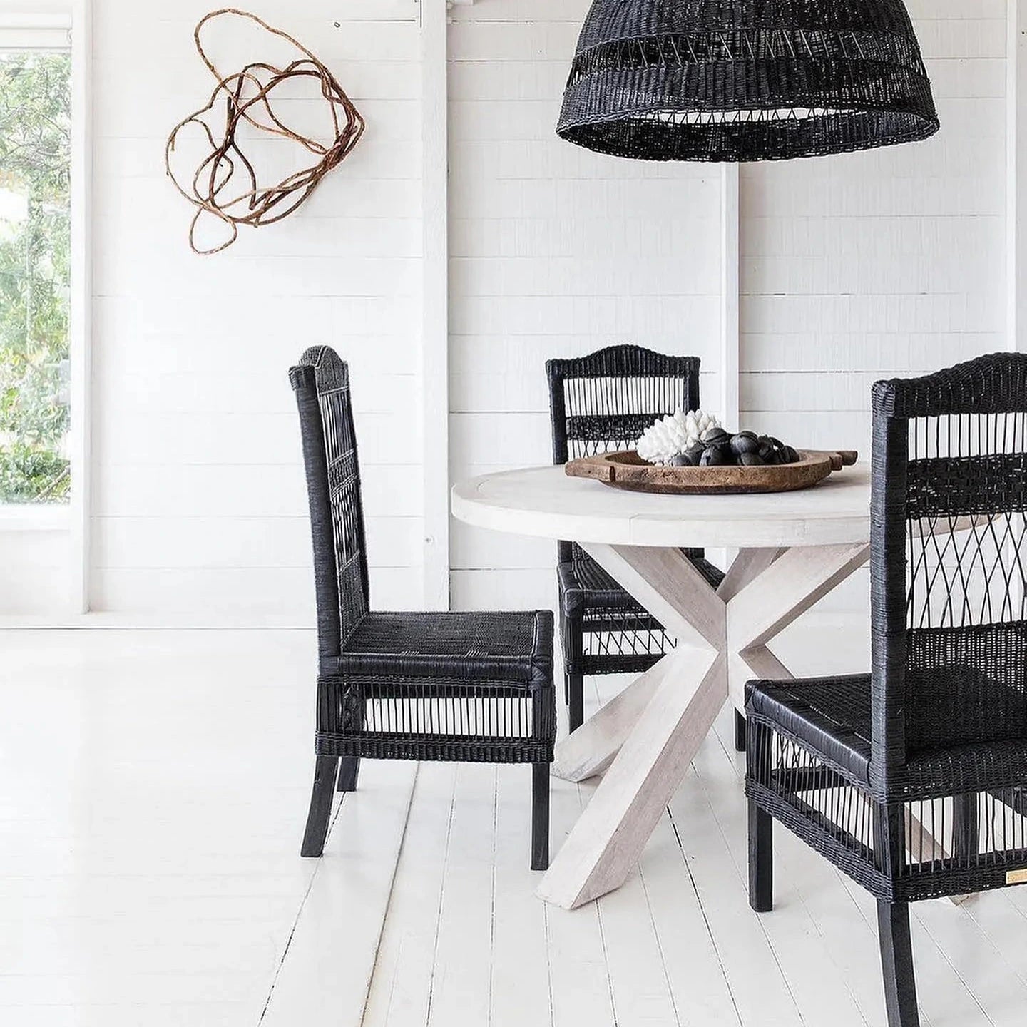 Dining area with black wicker chairs and a round table under a black woven pendant light.