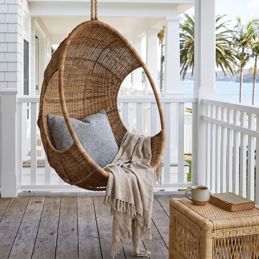Woven hanging chair on a porch with a blanket and cup, palm trees in the background