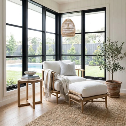 Cozy living room with a wooden armchair, ottoman, and side table near large windows.