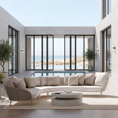 Modern outdoor living space with a curved sofa, coffee table, and large glass doors overlooking a pool and desert landscape.
