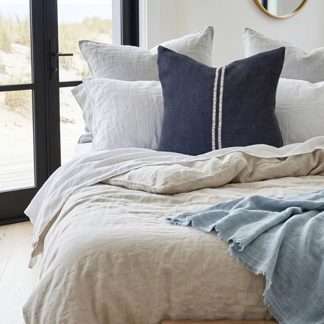 Neatly made bed with light-colored bedding and decorative pillows in a bright room.