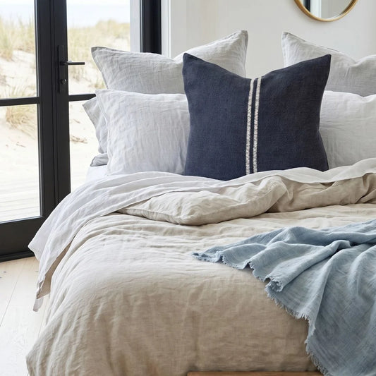 Neatly made bed with light-colored bedding and decorative pillows in a bright room.