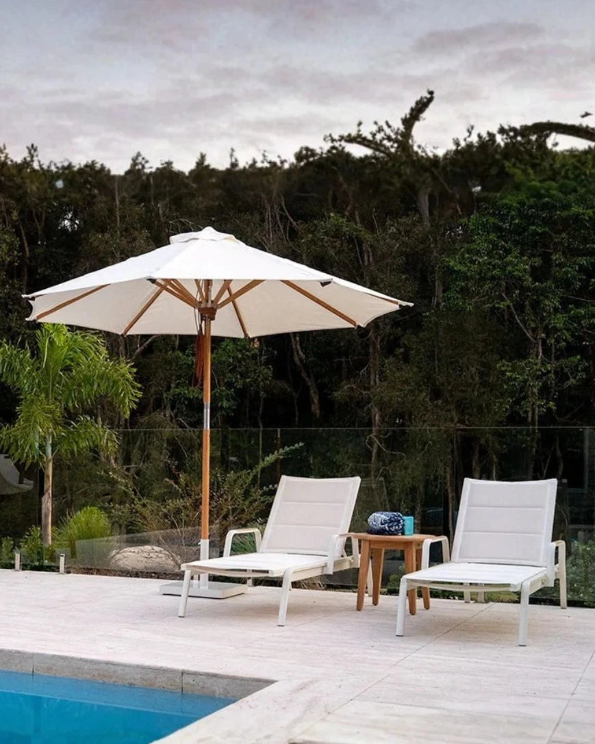 Outdoor patio with white chairs, table, and umbrella near a pool.