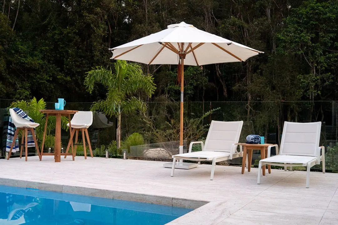 Poolside area with lounge chairs, table, and umbrella in a garden setting