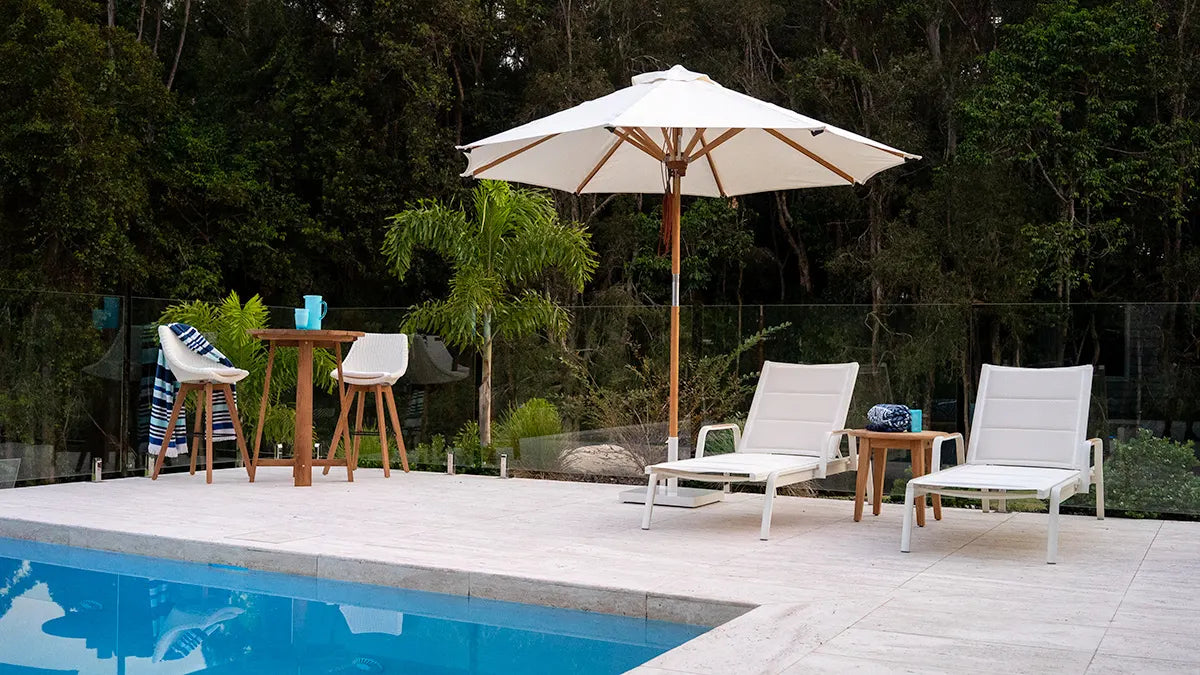 Outdoor patio area with pool, chairs, table, and umbrella in a garden setting.