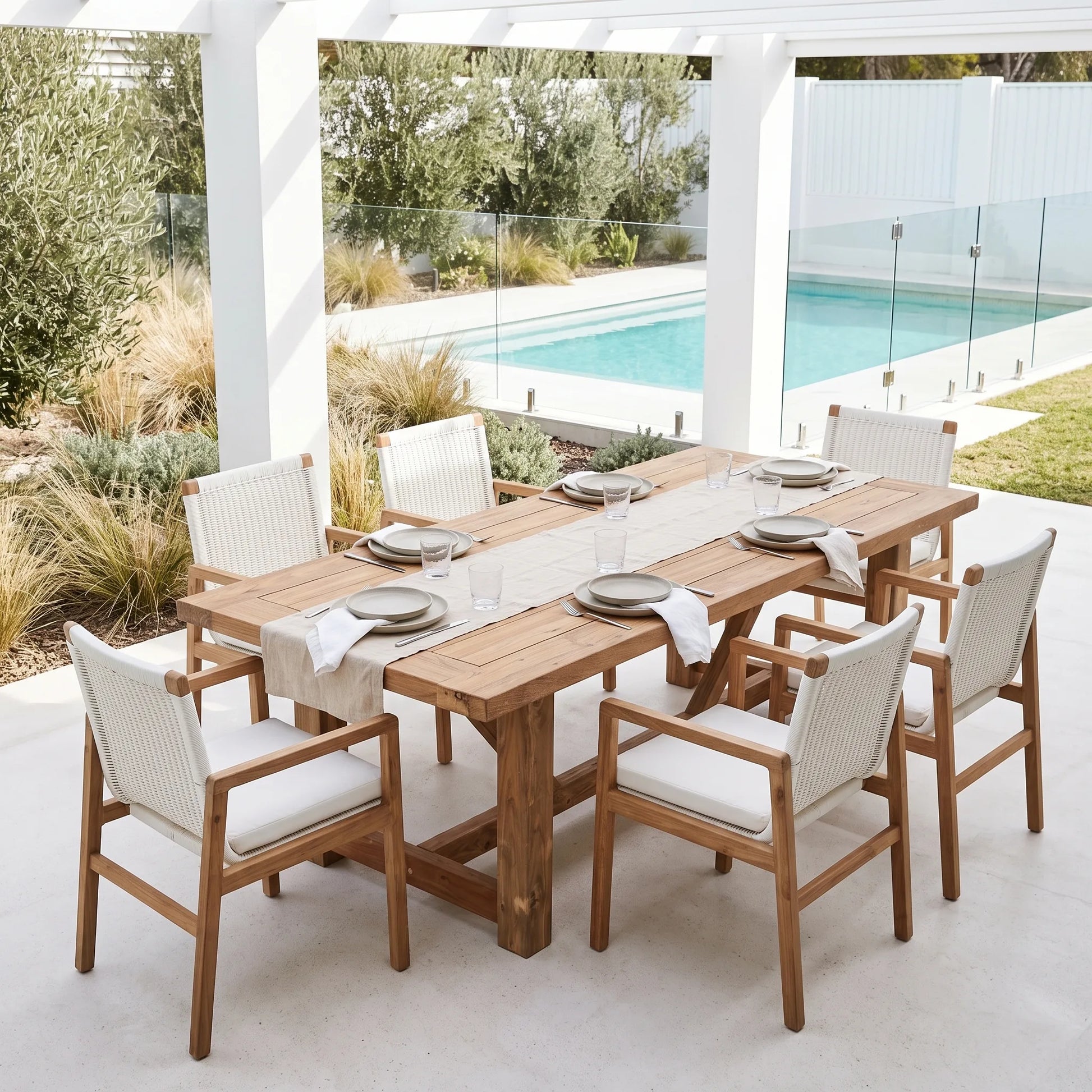A 7-piece outdoor dining set featuring a rectangular wooden table and six matching armchairs with white woven rope seats, set on a patio next to a swimming pool.