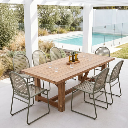 A rectangular wooden dining table with a rustic finish is set under a white pergola with six woven metal and cane chairs, overlooking a swimming pool in a backyard setting.