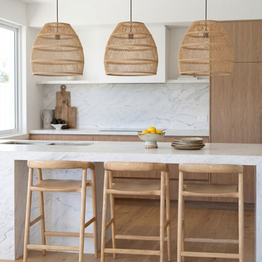 Modern kitchen with marble island, wooden stools, and wicker pendant lights.