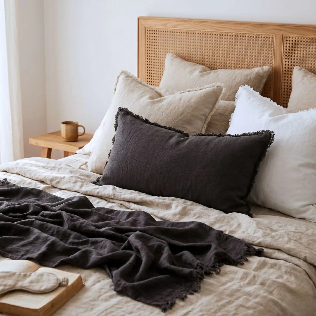 Bed with wooden headboard, pillows, and dark throw blanket in a bedroom setting.