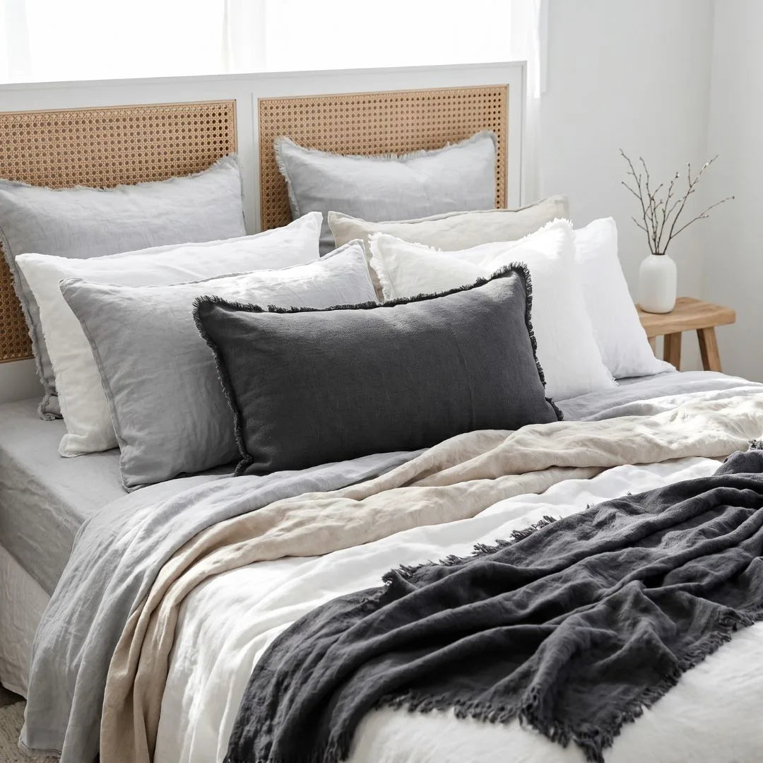 Bed with layered bedding and pillows against a neutral headboard.