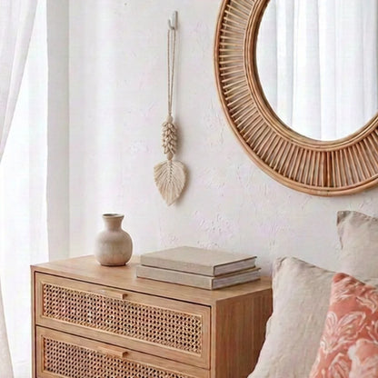 A light natural wood chest of drawers with woven cane panels, styled in a bedroom setting next to a round rattan mirror and a small vase.