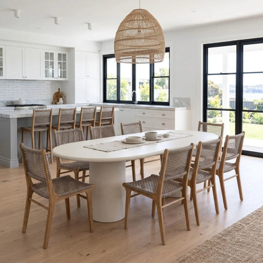 Dining area with a white microcement oval table and wooden chairs in a modern kitchen.