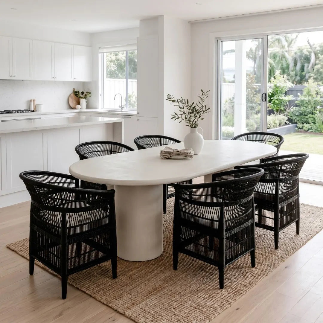 Modern kitchen with a white microcement dining table and black chairs, featuring a vase with plants.