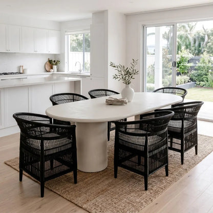 Modern kitchen with a white microcement dining table and black chairs, featuring a vase with plants.