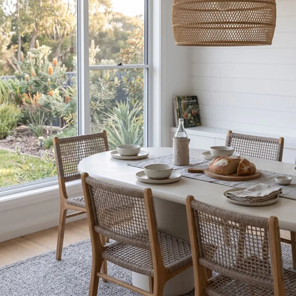Dining area with a oval table and wicker chairs, featuring a bottle, plates, and bread.