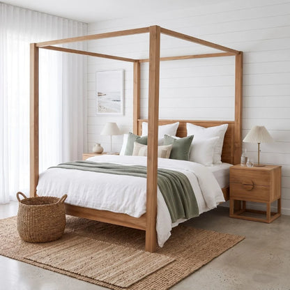 A light natural wood four-poster canopy bed with white bedding and sage green accents, styled in a bright, modern bedroom with a matching wood nightstand, woven basket, and shiplap wall.