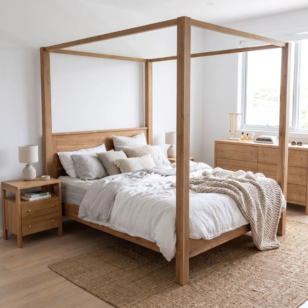 A light natural wood four-poster bed frame with white and beige bedding, styled in a bright, modern bedroom with a matching wooden nightstand and dresser.