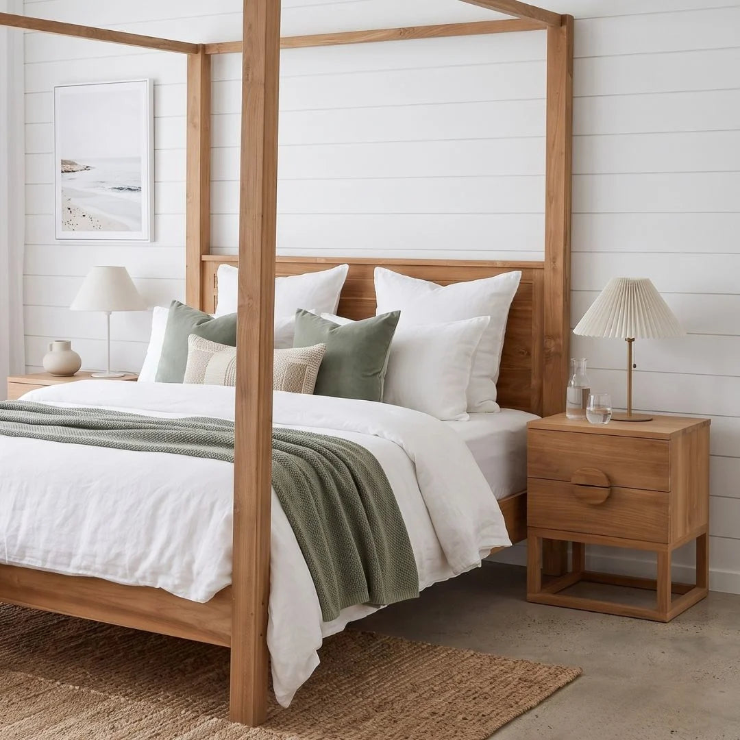 A light natural wood four-poster bed with white bedding, sage green pillows, and a sage green throw blanket, styled in a bright, modern bedroom with white shiplap walls, matching wood nightstands, and lamps.