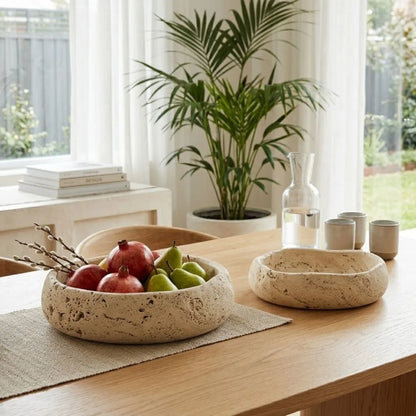 Natural Travertine Bowl with fruits on a wooden table in a bright room with plants and books.