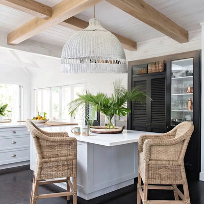 Modern kitchen with white island, wicker chairs, and wooden beams.