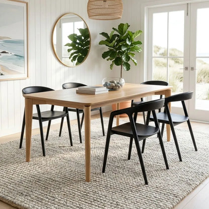 Dining room with wooden table and black chairs on a textured rug, large mirror, and plants.
