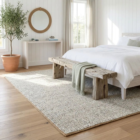 Bed room with wool and jute rug from Sun Republic, white bedding, and decorative elements.
