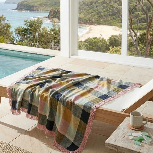 Colorful plaid blanket on a lounge chair by a pool with a scenic view of water and trees.