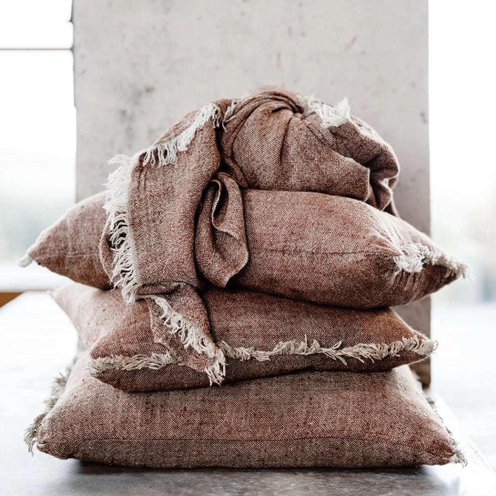 Stack of brown textured pillows with frayed edges on a light background