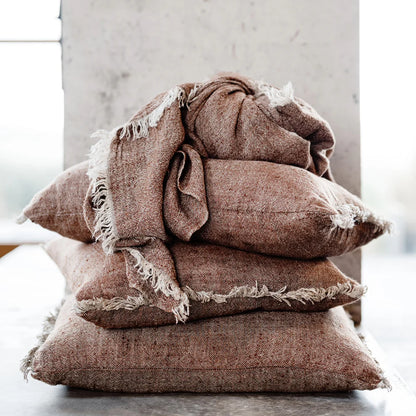 Stack of brown textured pillows with frayed edges on a light background