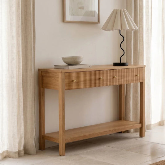 Wooden console table with a lamp and decorative items in a room with curtains and a painting.