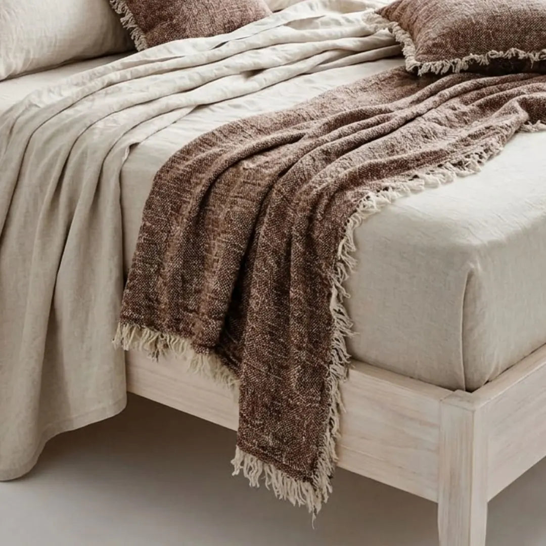 Neatly arranged bed with beige bedding and a brown textured throw blanket.