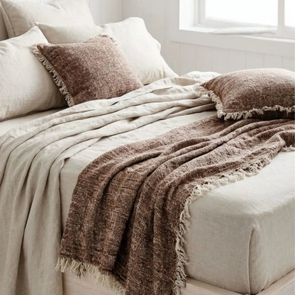 Neatly made bed with brown textured throw blanket and pillows in a bright room.
