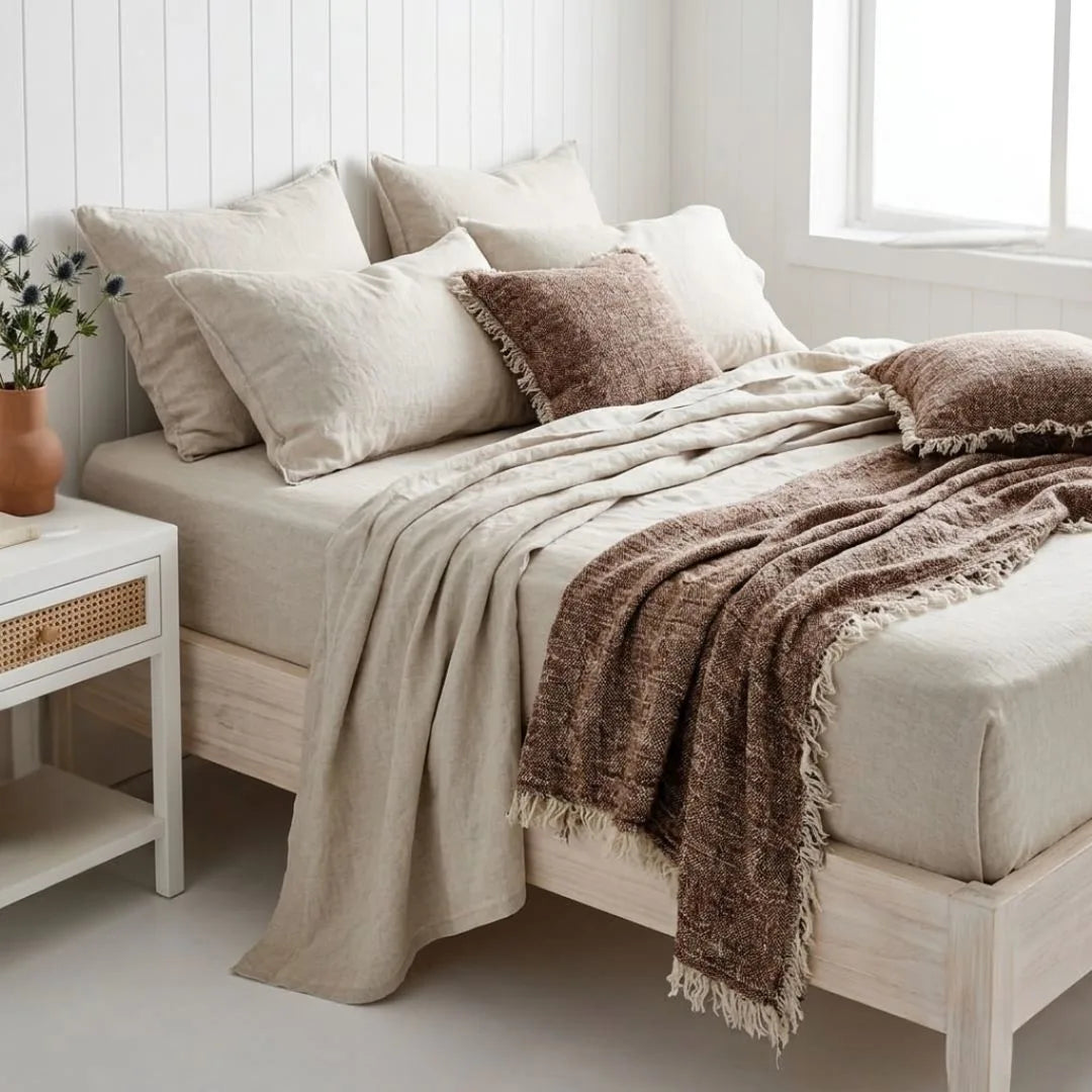 Neatly made bed with beige and brown bedding in a bright bedroom.