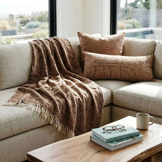 Beige sectional sofa with brown throw blanket and pillows in a living room setting.