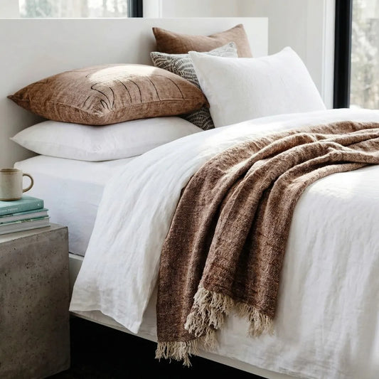 Bed with white linens, brown throw blanket, and pillows in a bedroom setting.