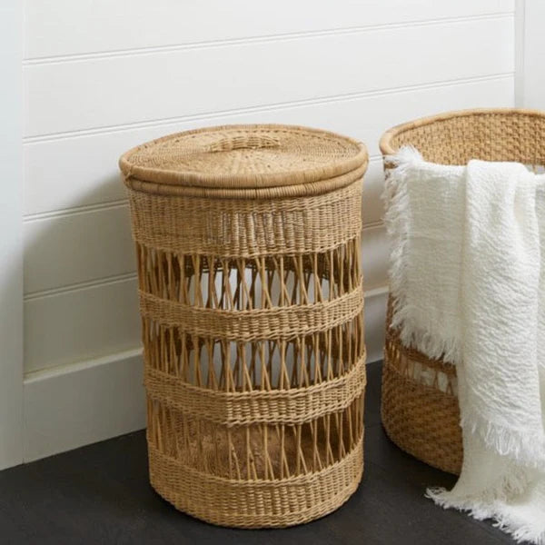Woven Cane laundry basket with a white towel draped over it against a white wall.