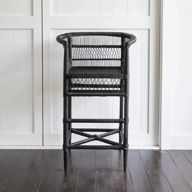 Black wicker chair against a white paneled wall.