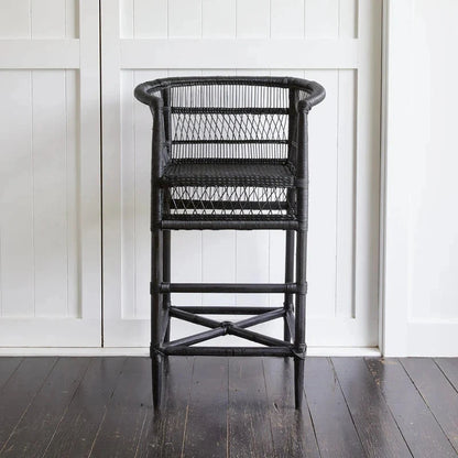 Black wicker chair against a white paneled wall.