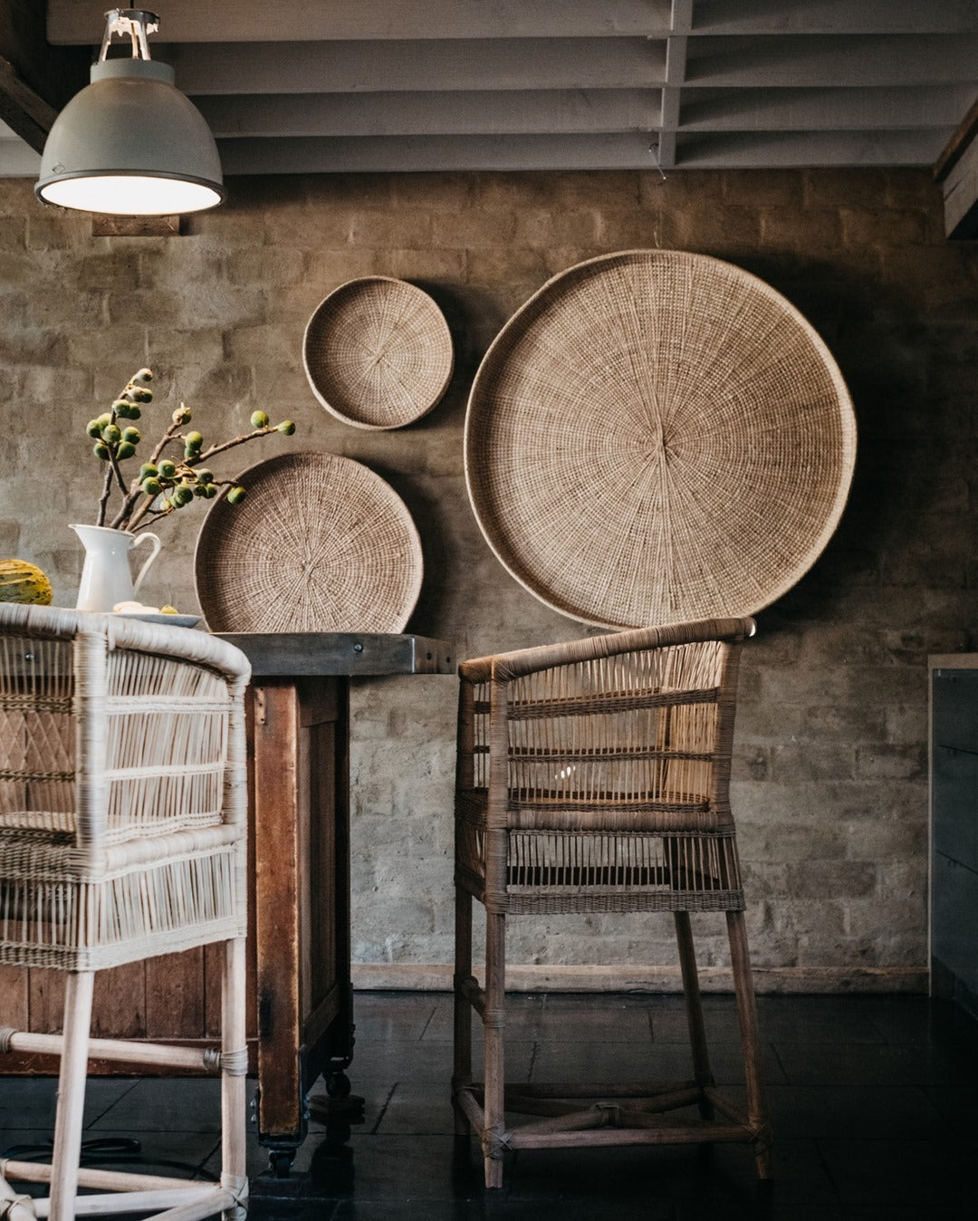 Woven baskets on a table against a textured wall with wicker chairs.