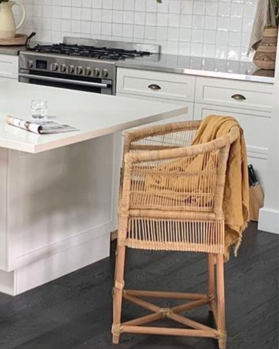 Kitchen with a wicker stool draped with a yellow cloth, white cabinets, and a tiled backsplash.