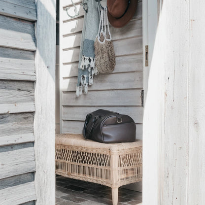 Brown leather bag on a wicker bench with a wooden wall and hanging items in the background
