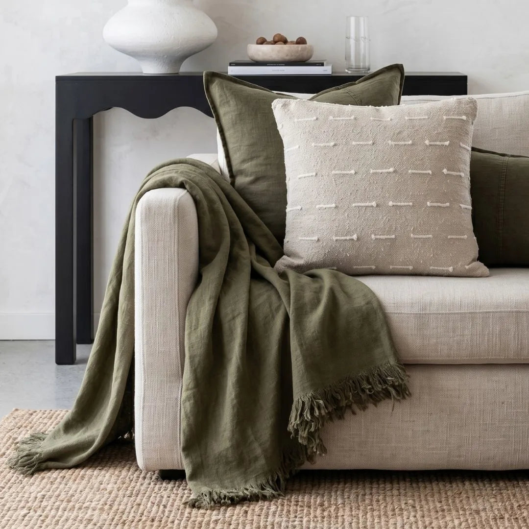Beige sofa with green throw blanket and beige pillow in a living room setting