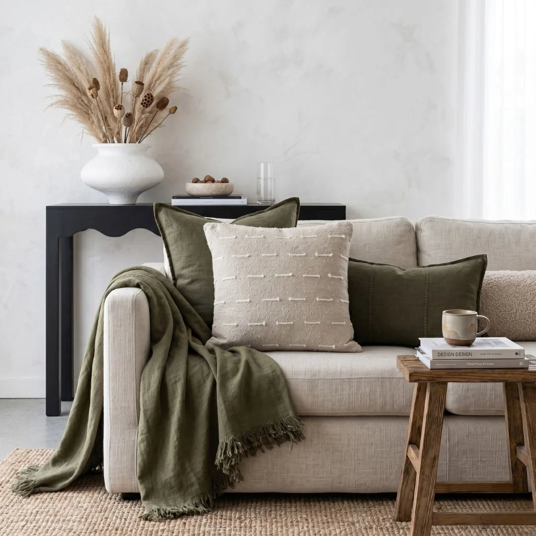 Cozy living room with a beige sofa, green blanket, and decorative pillows.