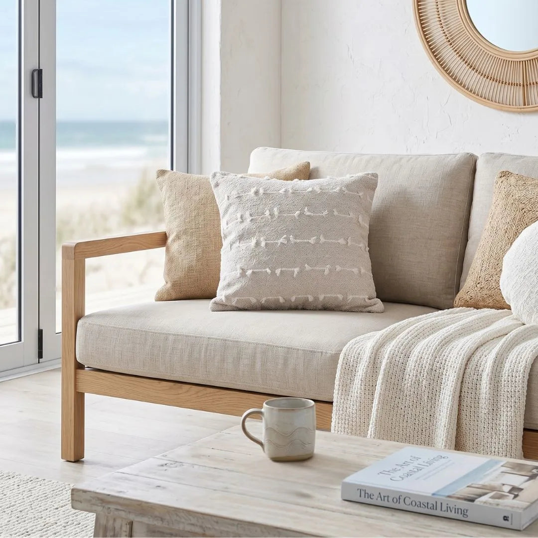 Beige sofa with decorative pillows and a coffee table in a living room with a view of the ocean.